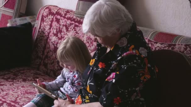Niña está sentada junto a su abuela en el sofá y viendo la foto — Vídeos de Stock
