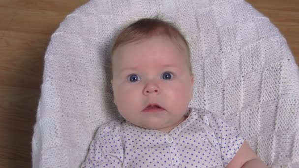 Un petit bébé joyeux est allongé sur une couverture en tricot blanc — Video