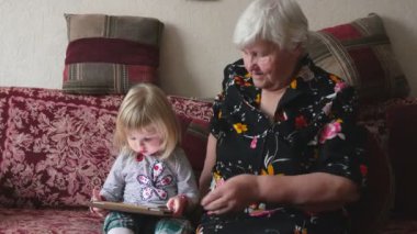 Küçük sevimli kız tablette büyükannesinin aile fotoğrafını gösteriyor.