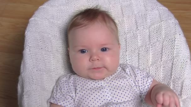 A cute baby in a white polka-dot costume is laying on a white knitted blanket — Stock Video