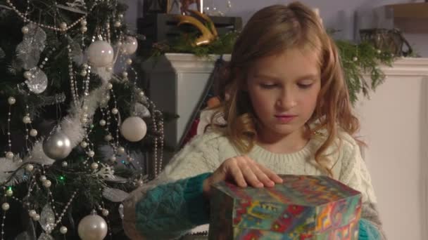 Verrast 8 jaar oud meisje opent geschenkdoos naast de kerstboom — Stockvideo