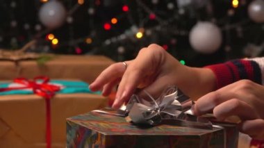 Eller Noel ağacının arka planındaki hediye kutusuna fiyonk koyuyor.
