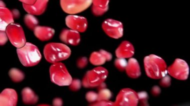 Sulu kırmızı olgun nar tanelerinin yakın çekimi siyah arkaplanda zıplıyor.