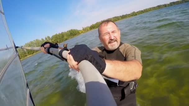Barbudo hombre va a navegar en una tabla de windsurf en un lago — Vídeos de Stock