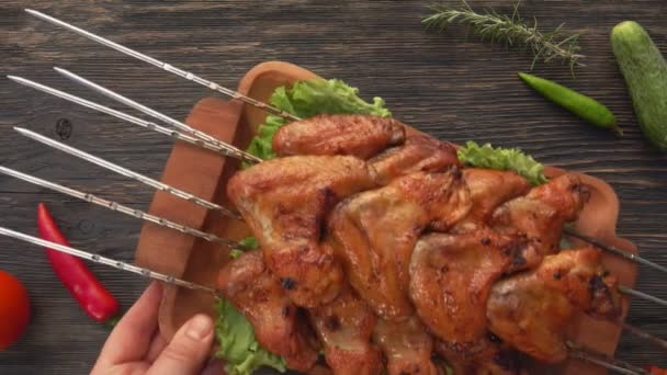 Şişlerin üzerinde lezzetli kızarmış tavuk kanatlarıyla dolu ahşap bir tabağın üst görüntüsü. — Stok video