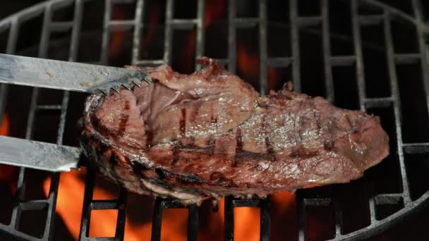 Kitchen tongs are flipping a beef steak lay on the grill grid — Vídeo de Stock