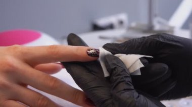 Siyah eldivenli manikürcü manikürü bitirdikten sonra oje sürüyor.