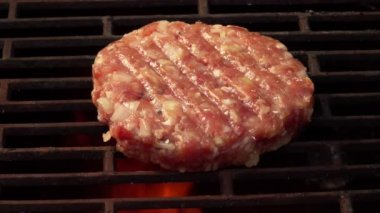 Çiğ hamburger pirzolasının üst görüntüsü açık ateşin üstündeki ızgara ızgarasında kızarıyor.