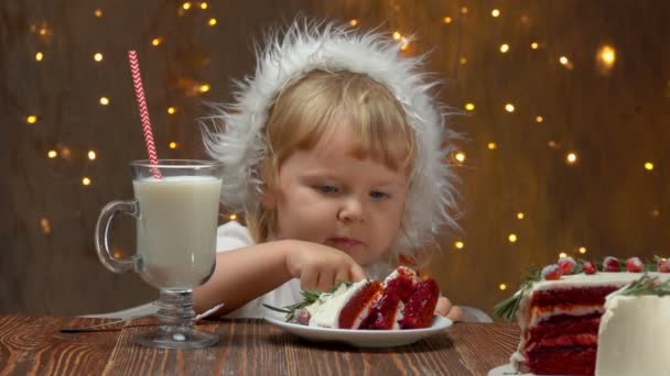 Mädchen mit roter Nikolausmütze isst roten Samtkuchen und trinkt Milch — Stockvideo