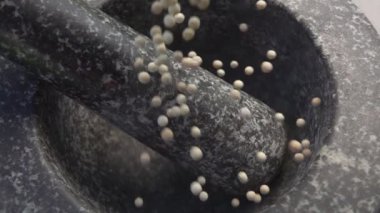 Baharatlı egzotik beyaz biberler gri taş havan topuna dökülüyor.