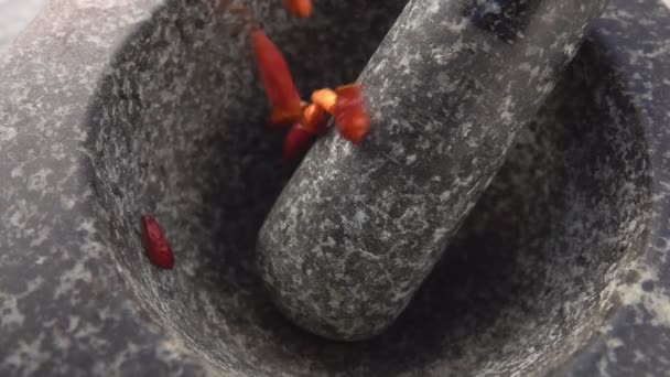 Super close-up of red cayenne pepper pods falling into the stone mortar — Stock Video