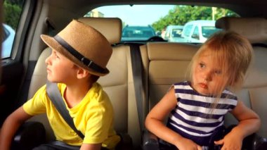 Küçük bir oğlan ve sarışın bir kız arabanın arka koltuğundalar.