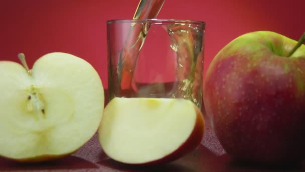 Taze elma suyu kırmızı arka plandaki bir bardağa yavaş çekimde dökülür. — Stok video