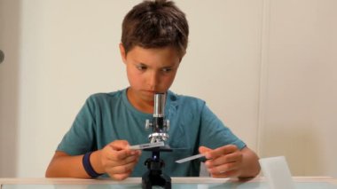 Bronzlaşmış bir çocuk mikroskopla objelere bakıyor.