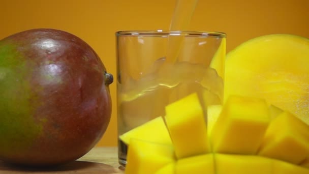 Γλυκό χυμό μάνγκο χύνεται σε ένα ποτήρι στο κίτρινο φόντο — Αρχείο Βίντεο