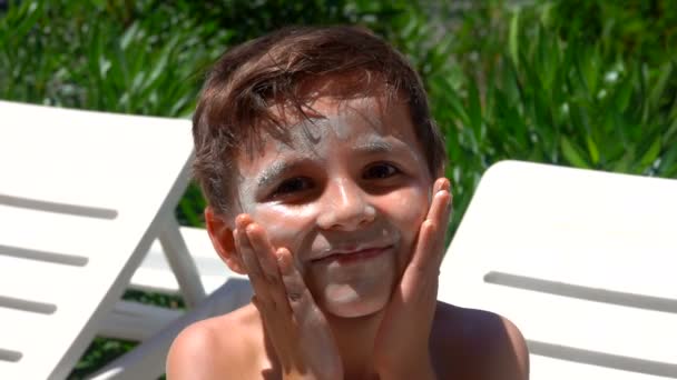 Menino bronzeado manchado com um creme de proteção solar está olhando para a câmera — Vídeo de Stock