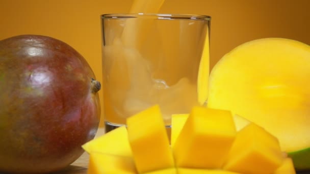 Mango juice hälls i ett glas bredvid en stor mogen mango skuren i kuber — Stockvideo