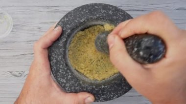 Erkek eller bir tokmakla havanda tuz, limon ve esmer şeker öğütüyor.