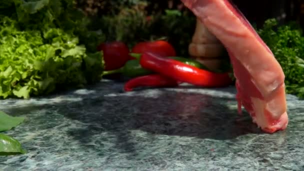 Filete crudo está cayendo sobre una mesa de piedra en el fondo de verduras frescas — Vídeos de Stock