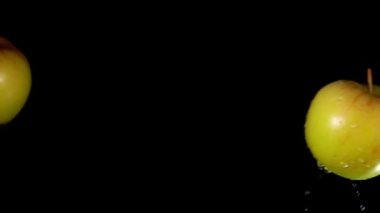 İki sarı elma yavaş çekimde siyah bir zeminde çarpışıyor.