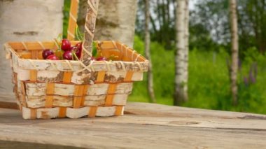 Kırmızı kiraz dolu bir sepet ağır çekimde ahşap masaya düşüyor.