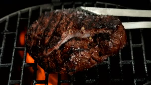 Kitchen tongs are flipping a delicious beef steak on the grill grid — Stock Video