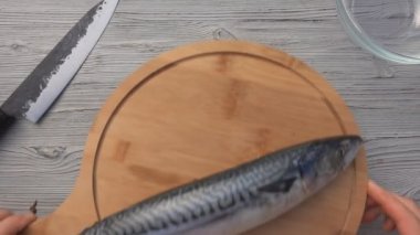 Erkek ellerinin üst görüntüsü yuvarlak ahşap tahtaya uskumru balığı koyuyor.