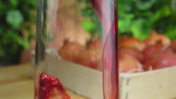 Panorama van granaatappelsap stroomt in een kruik op de achtergrond van groen — Stockvideo