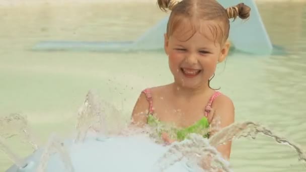 Маленька блондинка стукає по струмках води, що тече зі сфери фонтану — стокове відео