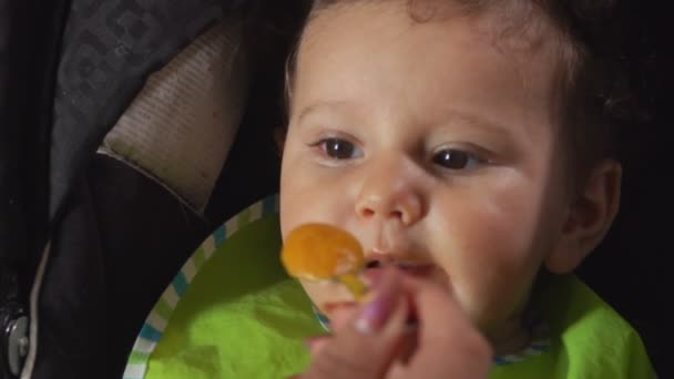 Кудрявые карие глазки маленький мальчик ест пюре овощей — стоковое видео