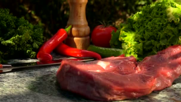 Råkött biff faller på ett stenbord på bakgrunden av färska grönsaker — Stockvideo