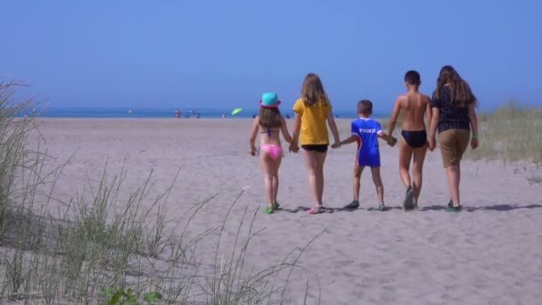 Vijf kinderen in heldere kleren rennen over het zand naar de zee. — Stockvideo