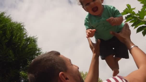 Happy father throws up a cheerful little curly baby boy outdoors — Stock Video