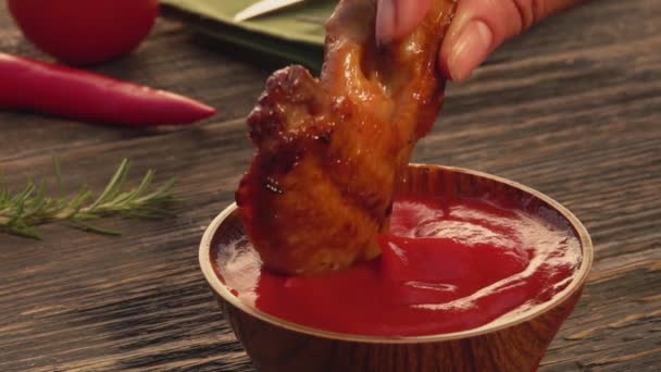 Primer plano de una mano hembra sumergiendo un ala de pollo a la parrilla en el ketchup — Vídeos de Stock