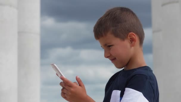 Menino bronzeado sorri e faz selfie no telefone ao ar livre — Vídeo de Stock