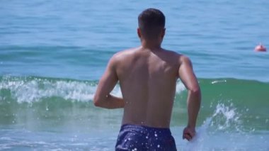 Genç yakışıklı adam deniz dalgalarına doğru koşuyor. 