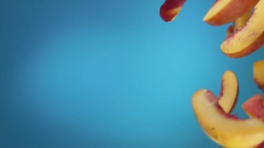 Taze olgun şeftali dilimleri mavi arkaplana çapraz düşüyor.
