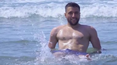 Genç yakışıklı adam dalgaların içinde kıyıda oturuyor.