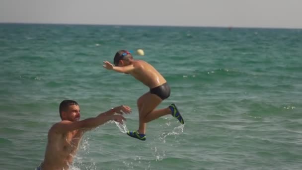 Unge pappa kastar pojken i havsvågorna. — Stockvideo