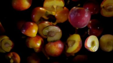 Olgun şeftali sineğinin yarıları siyah bir zemin üzerinde meyve suyu damlalarıyla döner.