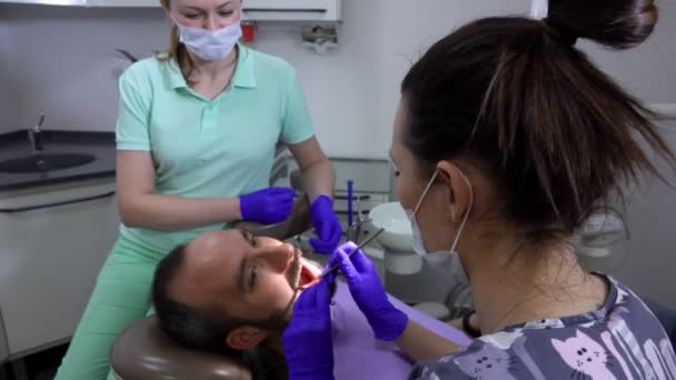 Жінка-стоматолог робить лікування зубів для пацієнта чоловічої статі — стокове відео