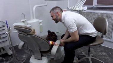 Küçük tatlı bir kız dişçi koltuğunda oturmuş dişçisini dinliyor.