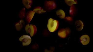 Islak şeftalinin yarısı siyah arkaplanda su damlalarıyla zıplıyor.