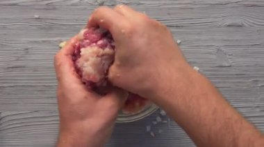 Cam bir kasede çiğ et, soğan ve baharatları karıştıran ellerin üst görüntüsü