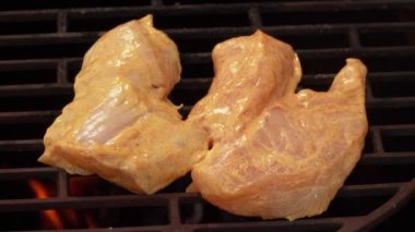 Çiğ tavuk filetosu ızgarada alevler içinde kızarıyor.
