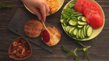 Kadın ellerinin tavuk filetosuyla ev yapımı ızgara burger yaparken üst görüntüsü.