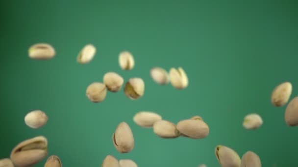 Close-up of salted pistachios flying and spinning on a green background — 비디오