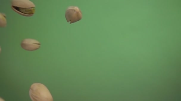 Närbild av saltade pistaschmandlar flyger diagonalt på en grön bakgrund — Stockvideo