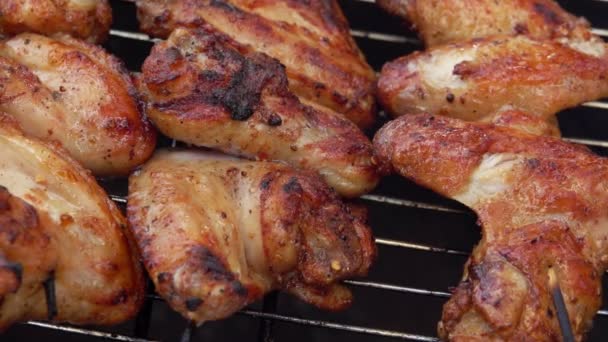 Primer plano de las sabrosas alas de pollo rotadas en la rejilla de la parrilla con pinzas metálicas — Vídeos de Stock