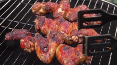 Tavuk kanatlarının yakın çekimi metal maşayla ızgara ızgarasında dönüyordu. 